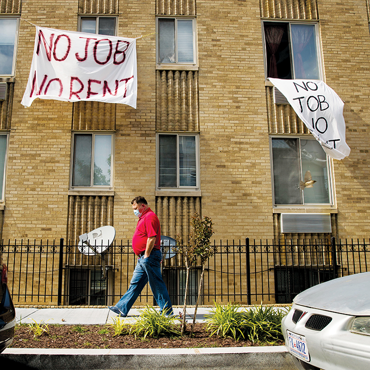 Man walking in front of a building with a sign that reads "No Job No Rent".