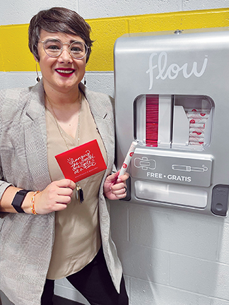 A woman front of a dispenser of free period products.